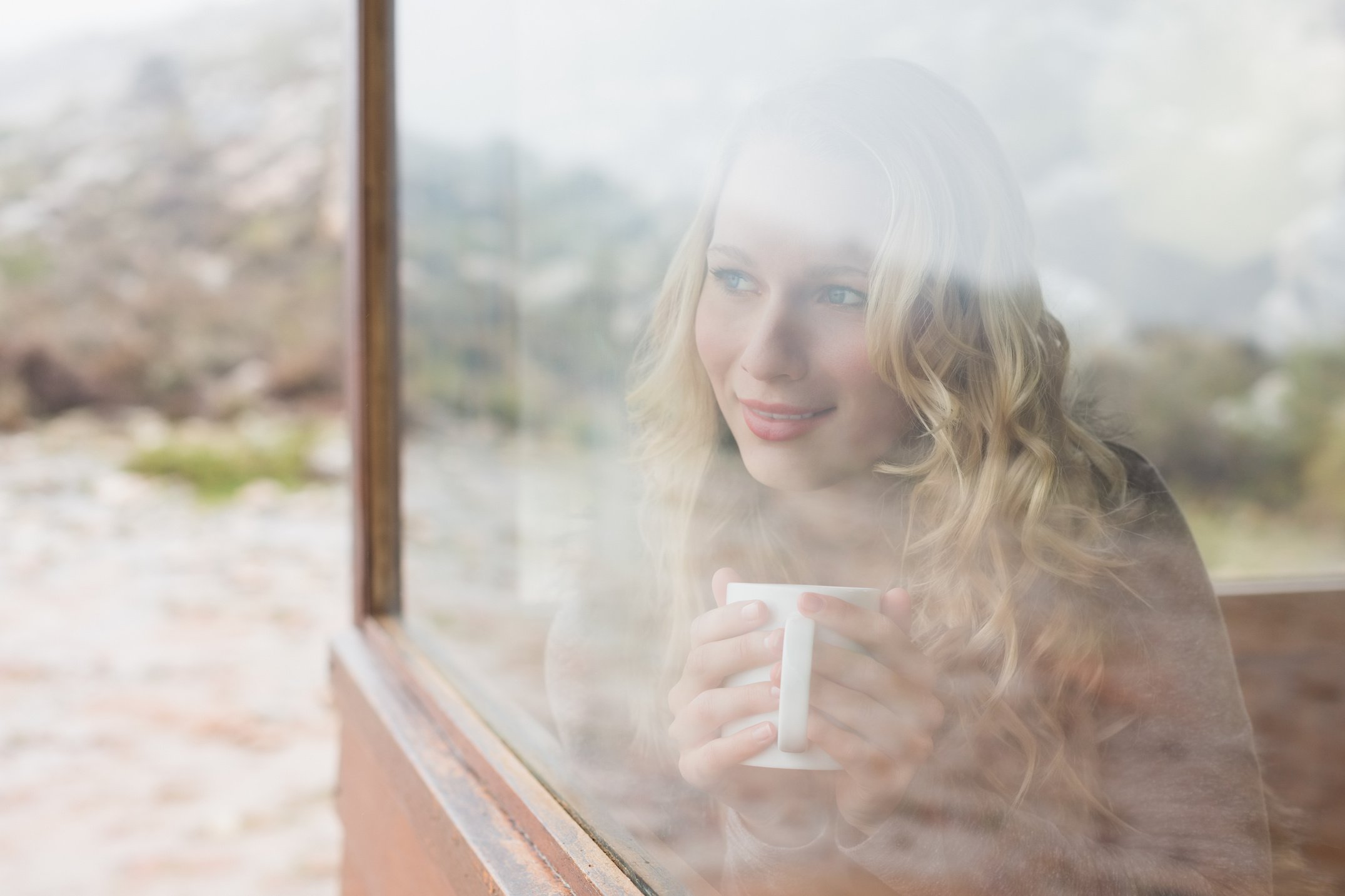 Woman with coffee cup looking out through cabin window